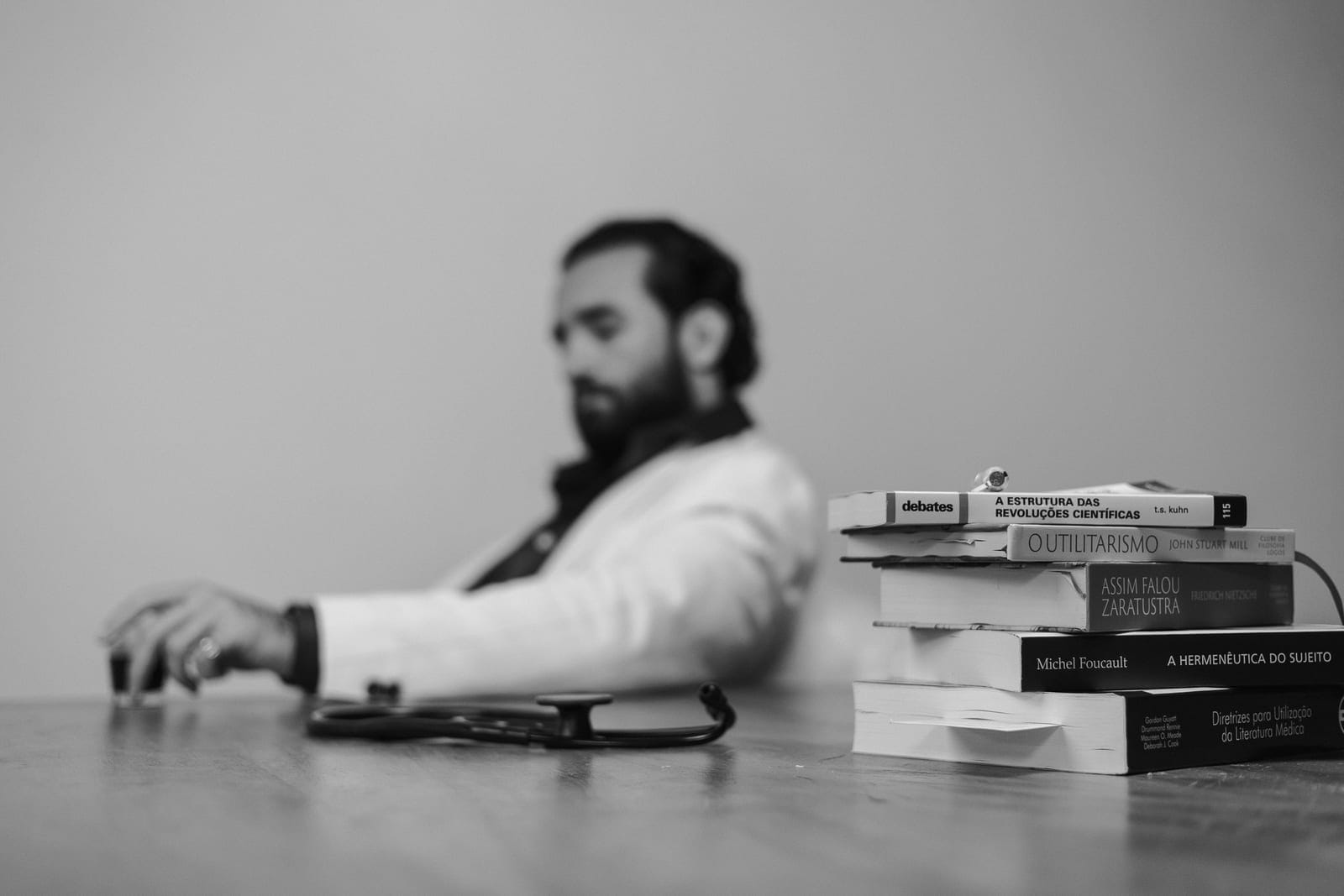 Dr. Eric Pascher à mesa, em preto e branco, com uma pilha de livros à frente